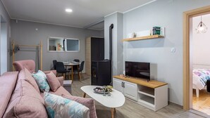 Un espace de vie compact comprenant un canapé, une table à manger, un téléviseur et une petite kitchenette.