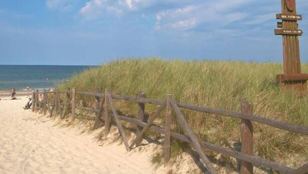 Une plage avec une clôture en bois et un panneau indicateur.