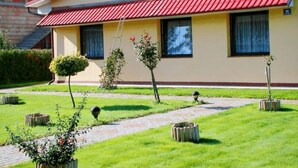 Un bâtiment à deux étages, avec un toit rouge et des murs de couleur beige, agrémenté d’un petit jardin doté d’un chemin pavé et de plusieurs plantes en pot.