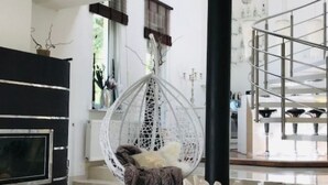 Una sala de estar moderna con una mesa de vidrio, una silla colgante, una araña y una chimenea.