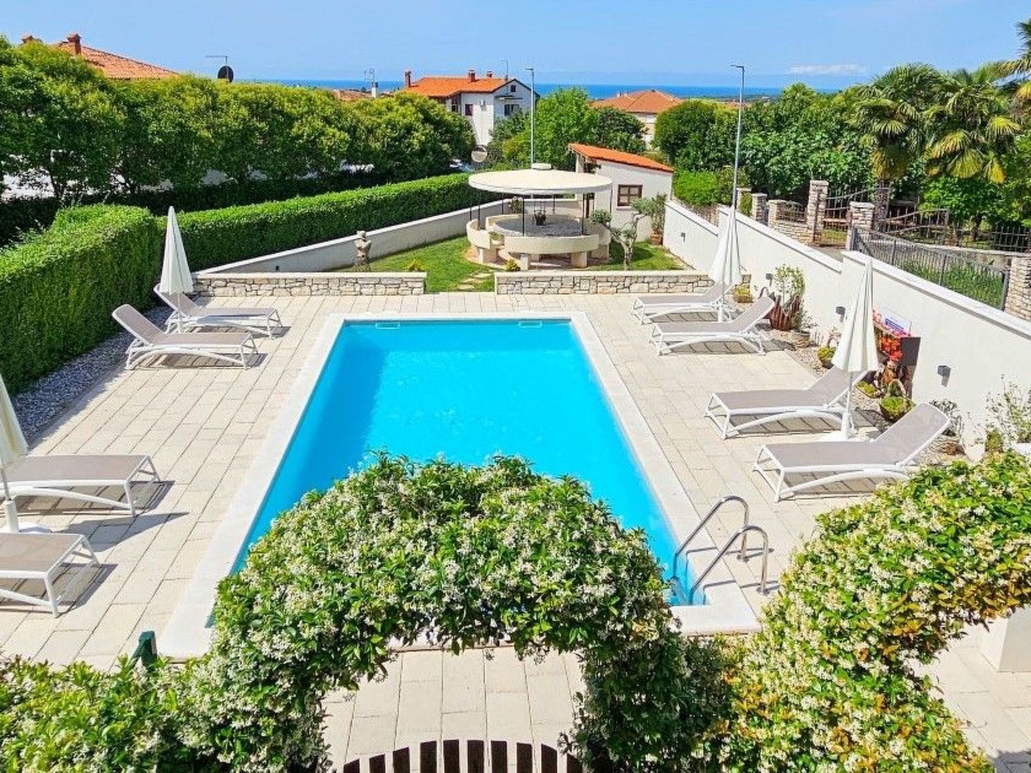 A rectangular swimming pool with a surrounding deck, lounge chairs, and a small circular seating area.