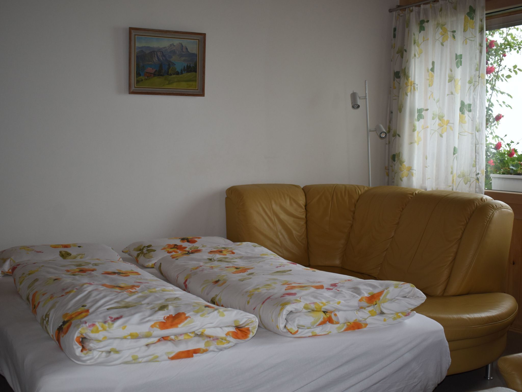 Ein Zimmer mit einem Bett, einer Couch, einem Gemälde an der Wand und einem Fenster mit Vorhängen.