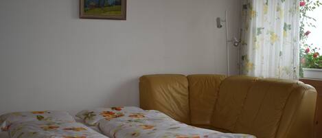 Ein Zimmer mit einem Bett, einer Couch, einem Gemälde an der Wand und einem Fenster mit Vorhängen.
