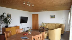 A cozy living room with a wooden ceiling, a flat-screen TV, a sofa, and a dining table with chairs.