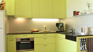 A kitchen with green cabinets, a built-in oven, a coffee maker, and a kettle.