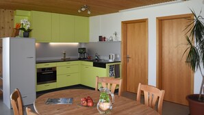 A modern kitchen with green cabinets, a wooden ceiling, and a dining area with a table and chairs.