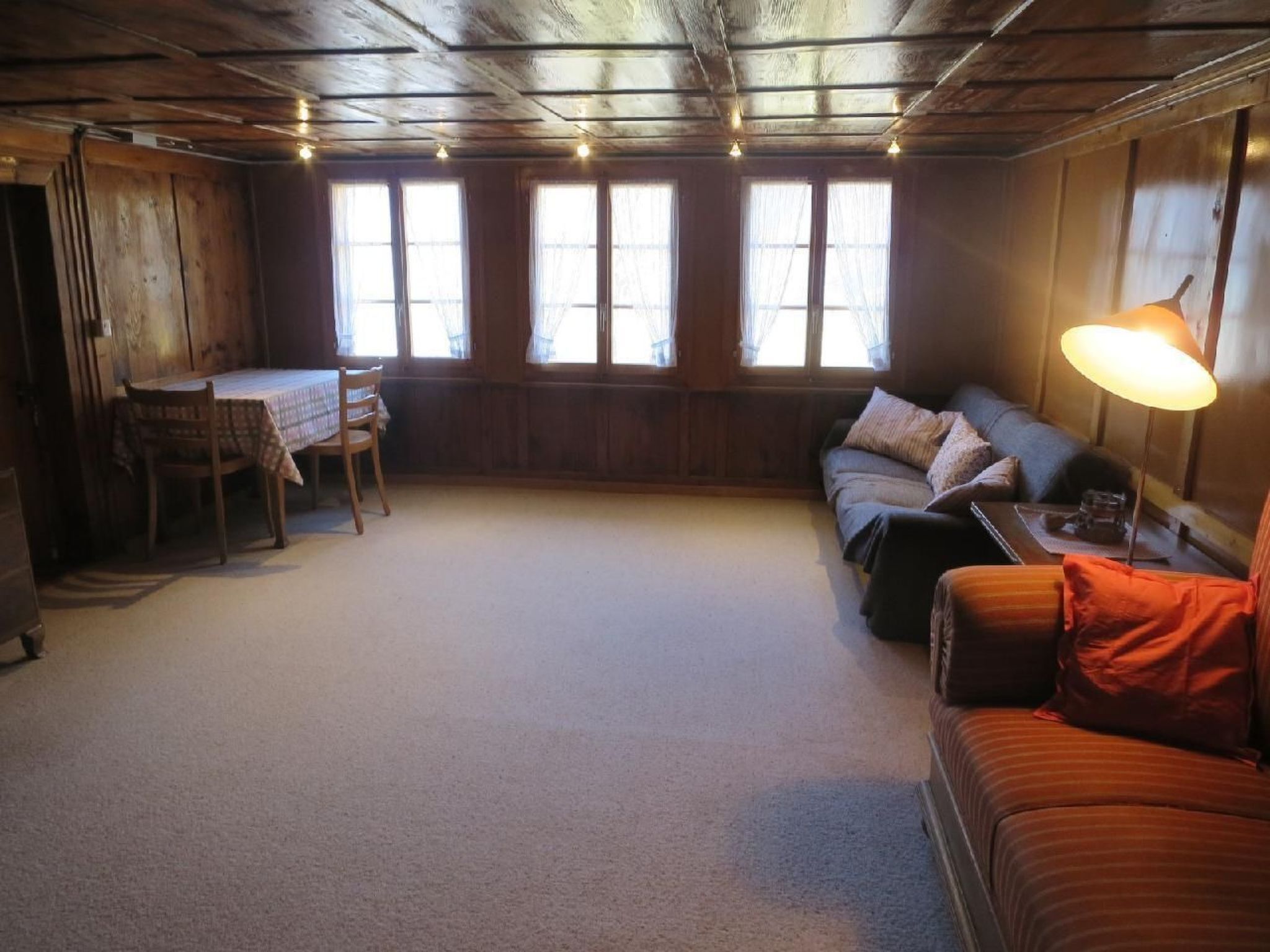Une pièce chaleureuse avec un plafond en bois, un canapé, une table avec des chaises et de grandes fenêtres.