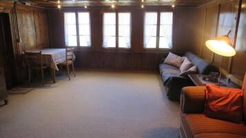 Une pièce chaleureuse avec un plafond en bois, un canapé, une table avec des chaises et de grandes fenêtres.