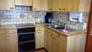 Eine kleine Küche mit Holzschränken, einem Geschirrspüler, einem Backofen, einer Spüle und einer Kaffeemaschine.