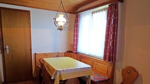 Ein kleiner, gemütlicher Raum mit Holztisch und Bank, einem Fenster mit karierten Vorhängen und einer Pendelleuchte.