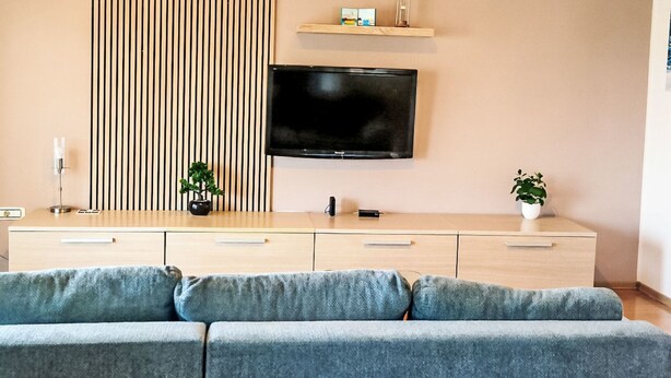 A modern living room with a flat-screen TV, a wooden cabinet with drawers, a sofa, and a vertical striped panel. - Appartement "Appartement Sarah" mit Balkon by Interhome (Buzdohanj)