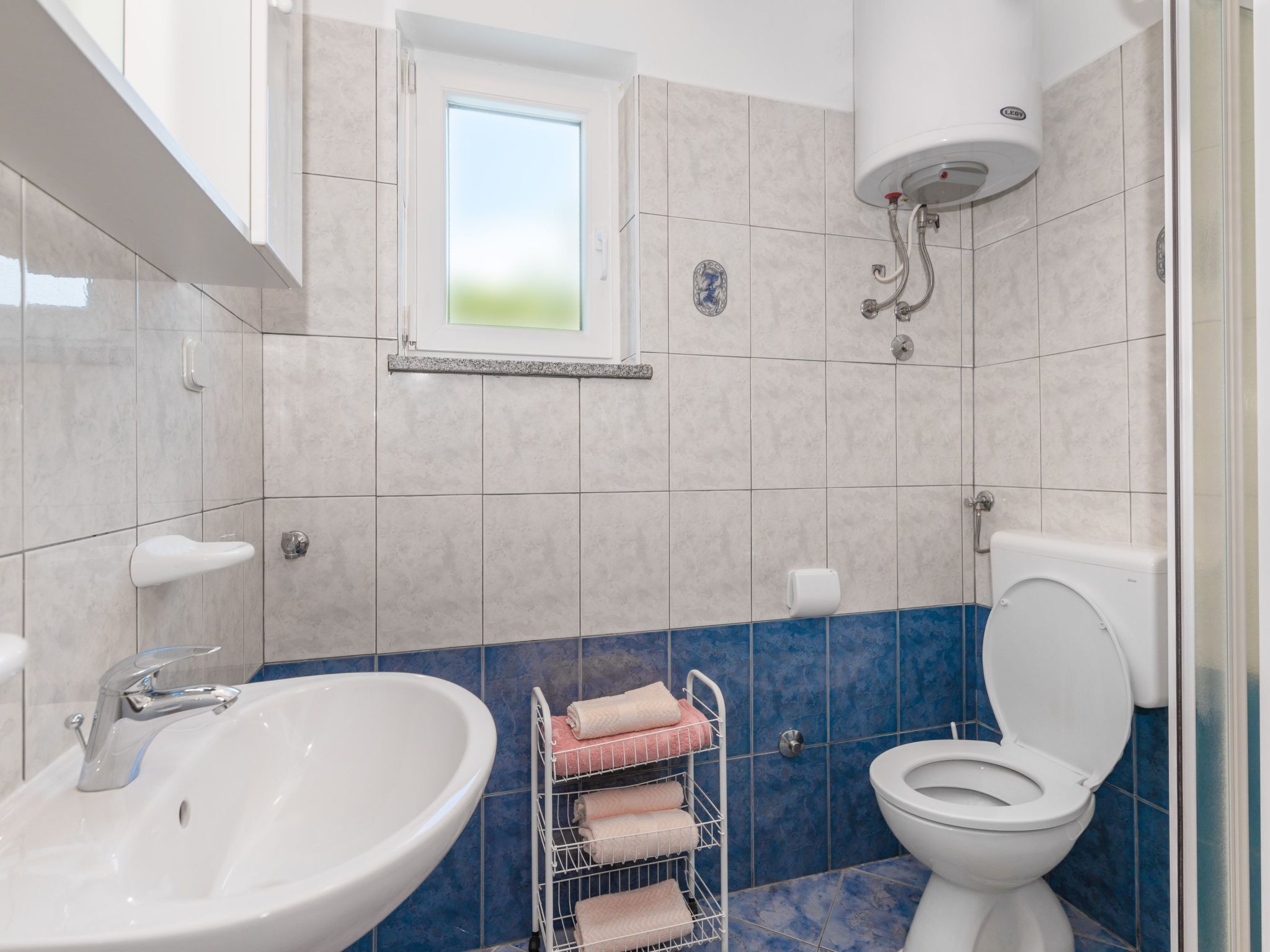 Een badkamer met een wastafel, toilet en een handdoekrek met handdoeken.