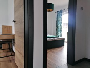 A modern room with a wooden desk, a bed with a green bedspread, and a window with curtains.