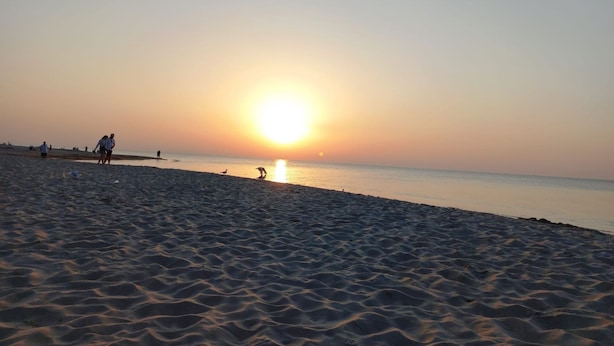Una playa al atardecer con gente caminando y de pie.