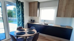 Una cocina moderna con una mesa redonda y sillas, una ventana con persianas y armarios de madera.