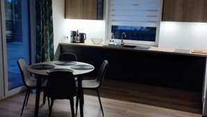 Una cocina moderna con comedor, que presenta una mesa redonda, sillas, una cafetera y un ventanal con persianas.