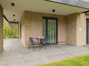 A modern outdoor patio area with a brick wall, a glass door, and a small round table with two chairs. - Wohnung für 4 Personen "Nowe Miedzywodzie" by Interhome (Miedzywodzie)
