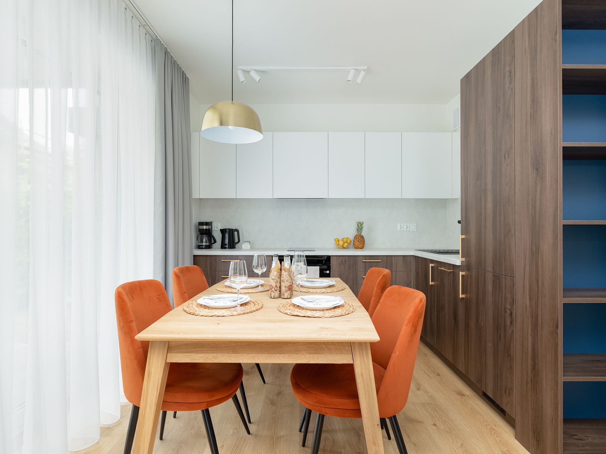 Une cuisine moderne avec une table à manger en bois, des chaises orange et un grand luminaire suspendu.