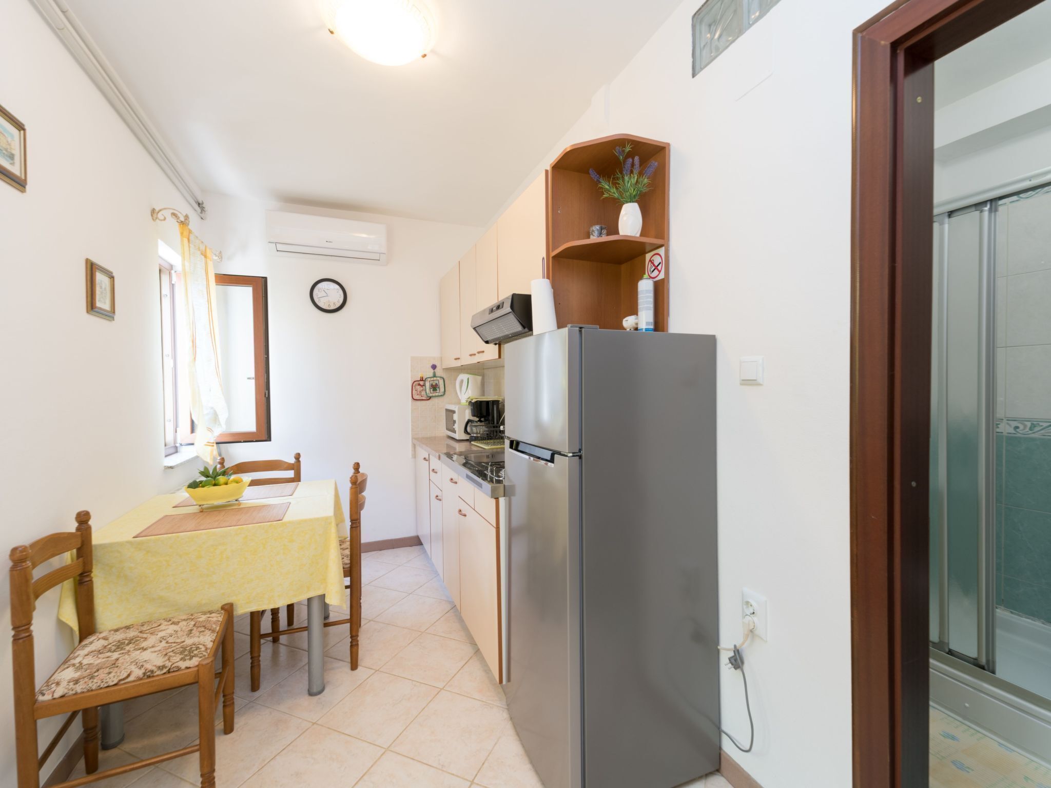 Cocina compacta con refrigerador, microondas y estufa. Hay una mesa de comedor con sillas y una ventana con cortinas.