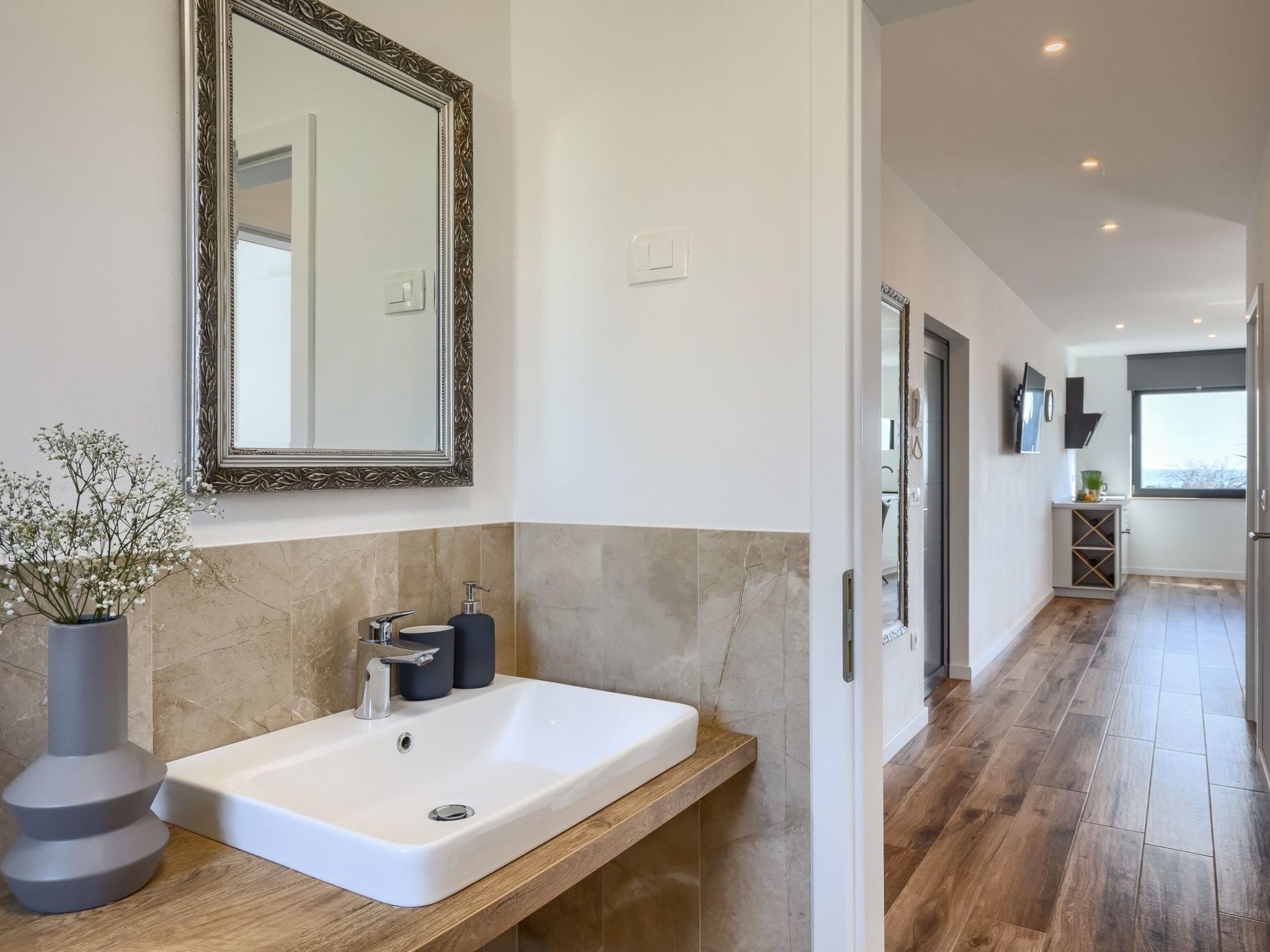 Un baño moderno con un espejo grande, un lavabo blanco y un mueble de tocador de madera.