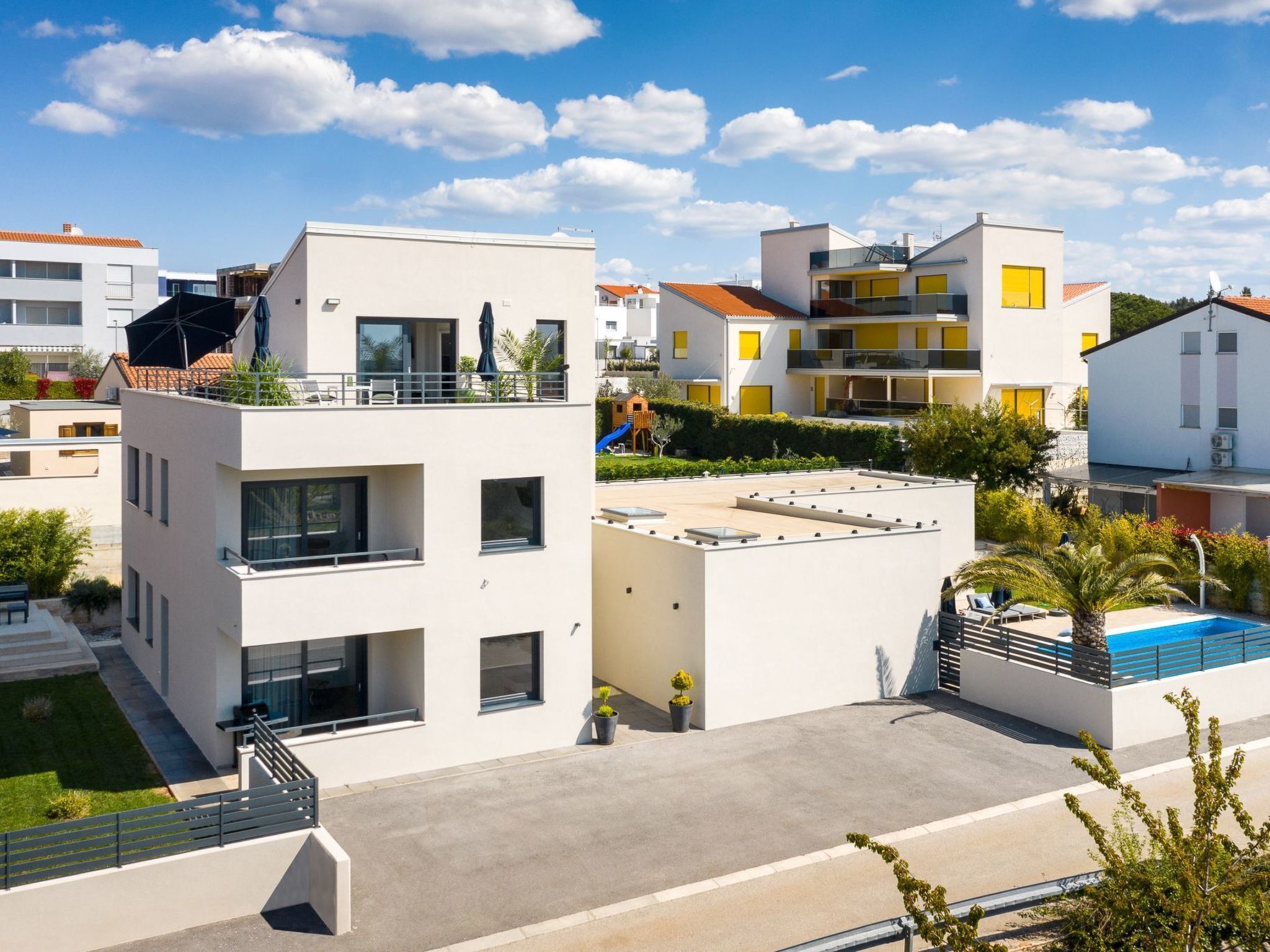 En modern bostadsbyggnad med ett platt tak, flera balkonger och en swimmingpool.