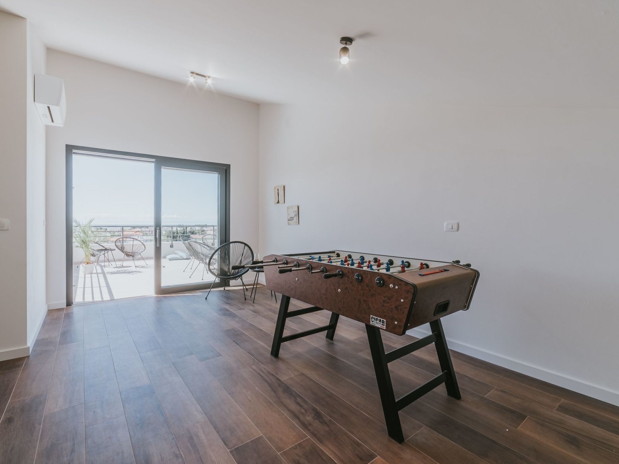 A spacious room with a foosball table, a sliding glass door leading to a balcony, and a modern interior design.
