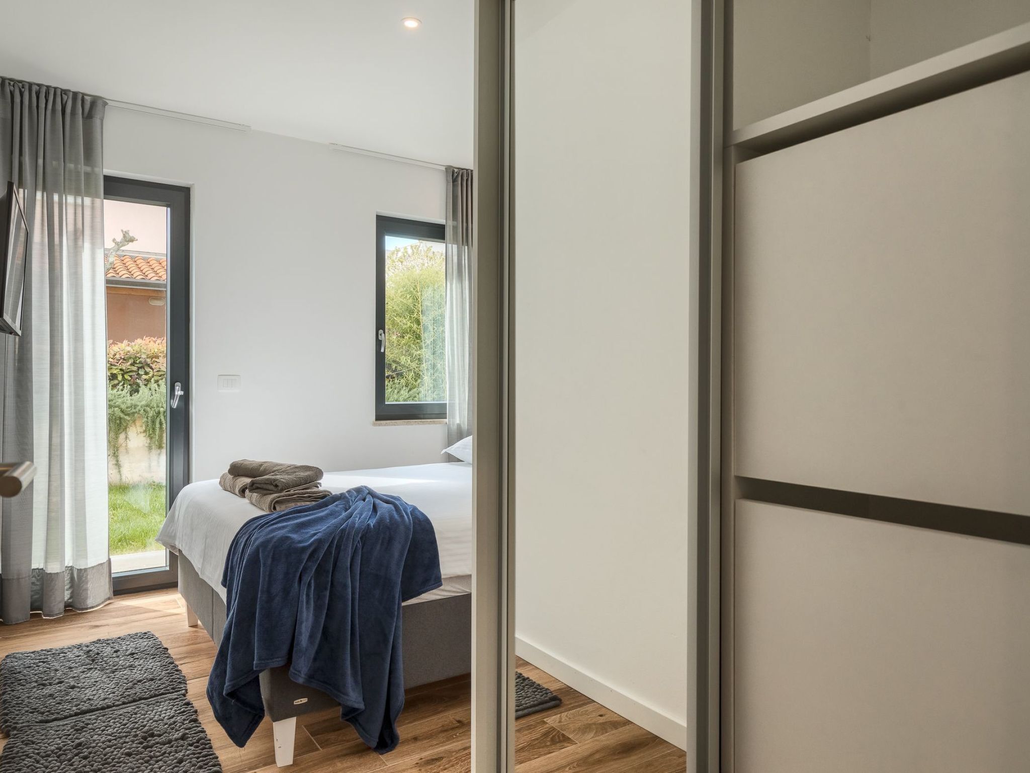 A modern bedroom with a bed, a window, and a sliding door to a balcony.