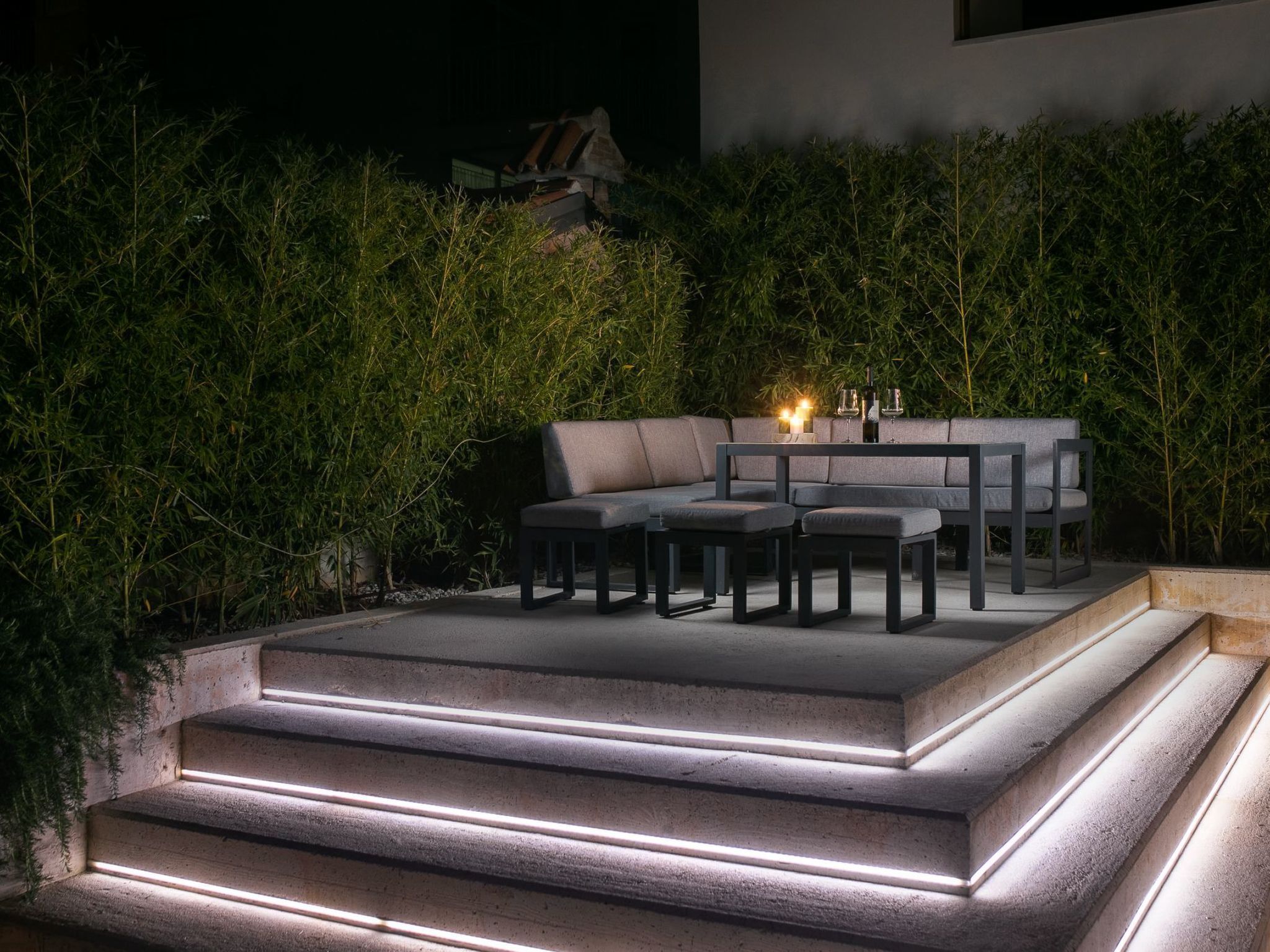 An outdoor seating area with a sofa and tables, surrounded by lush greenery.