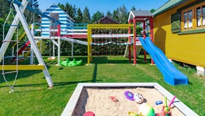 Une aire de jeux avec un toboggan, un filet d’escalade et des balançoires.
