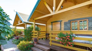 Une cabane en bois dotée d’un porche couvert, d’un escalier menant à l’entrée et d’un jardin agrémenté de diverses plantes et fleurs.
