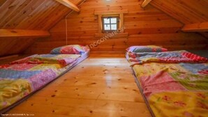 Une chambre confortable située dans les combles, avec des murs en bois et un plafond en pente, et comprenant deux lits dotés d’une literie aux couleurs vives.