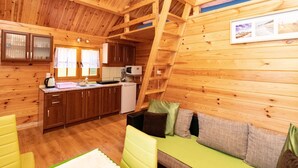 A wooden cabin interior with a kitchenette, a dining area, and a sofa with cushions. - in Rusinowo mit Terrasse und Garten by Interhome (Rusinowo)