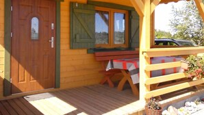 A wooden cabin with a wooden door, a window with shutters, a table with a red and gray tablecloth, and a bench. - Die Ostsee by Interhome (Rusinowo)