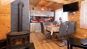 A cozy cabin interior with a wood stove, dining area, kitchen, and a TV mounted on the wall. - Die Ostsee by Interhome (Rusinowo)