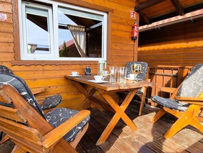 A wooden cabin with a dining area featuring a table and chairs, a window with curtains, and a fire extinguisher mounted on the wall. - "New 5" with Infinity-Pool by Interhome (Rusinowo)