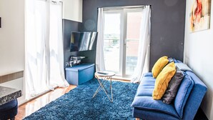 Ein modernes Wohnzimmer mit einem blauen Sofa, einem Flachbildfernseher, einem blauen Teppich und einem Balkon mit Vorhängen.