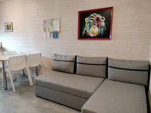 Ein modernes Wohnzimmer mit einer grauen Couch, weißen Sesseln, einem kleinen Tisch und einem farbenfrohen Gemälde an der Wand.