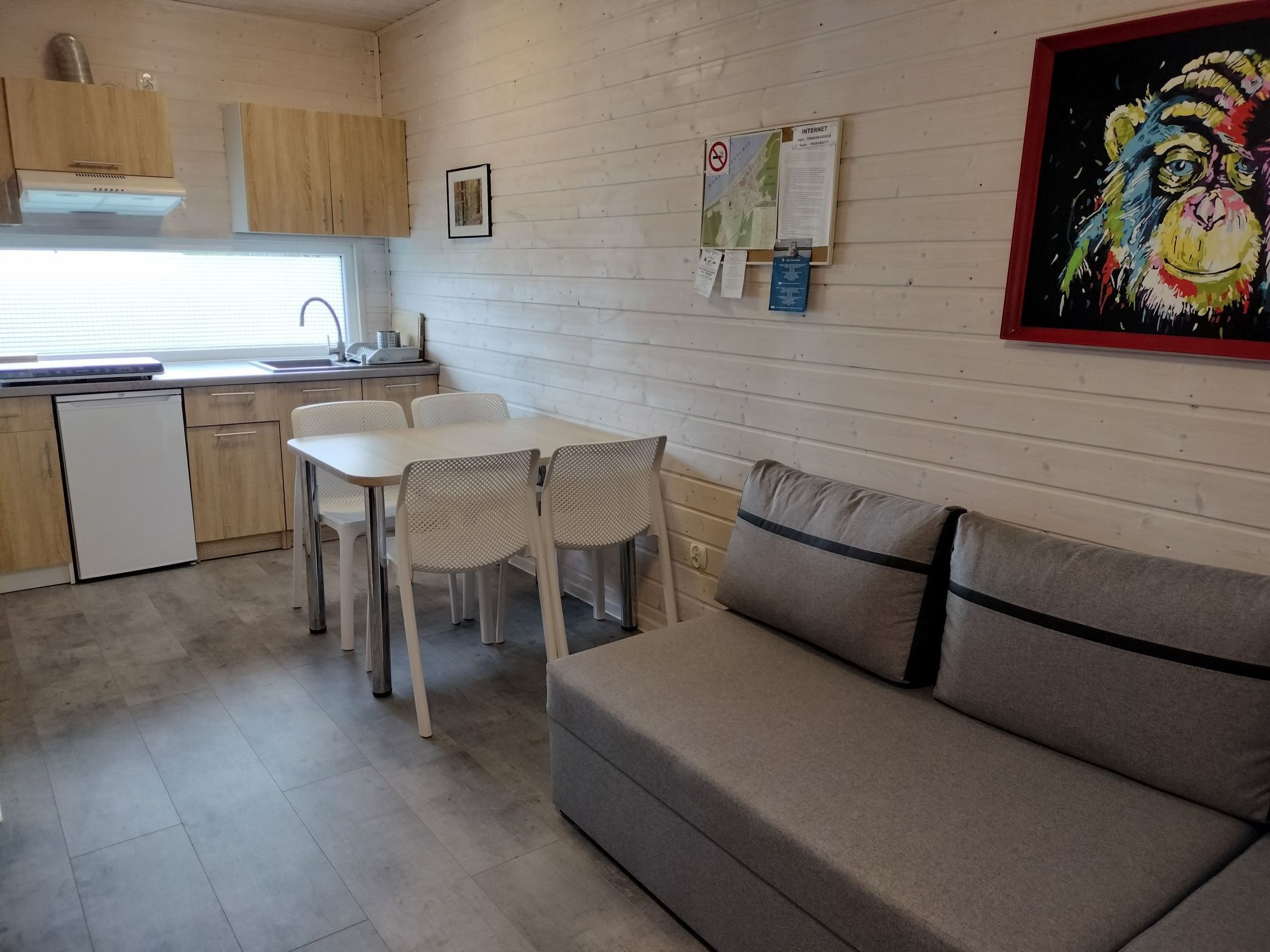 A compact kitchen with wooden cabinets, a white countertop, and a sink. There is a dining area with a table and chairs, and a sofa.