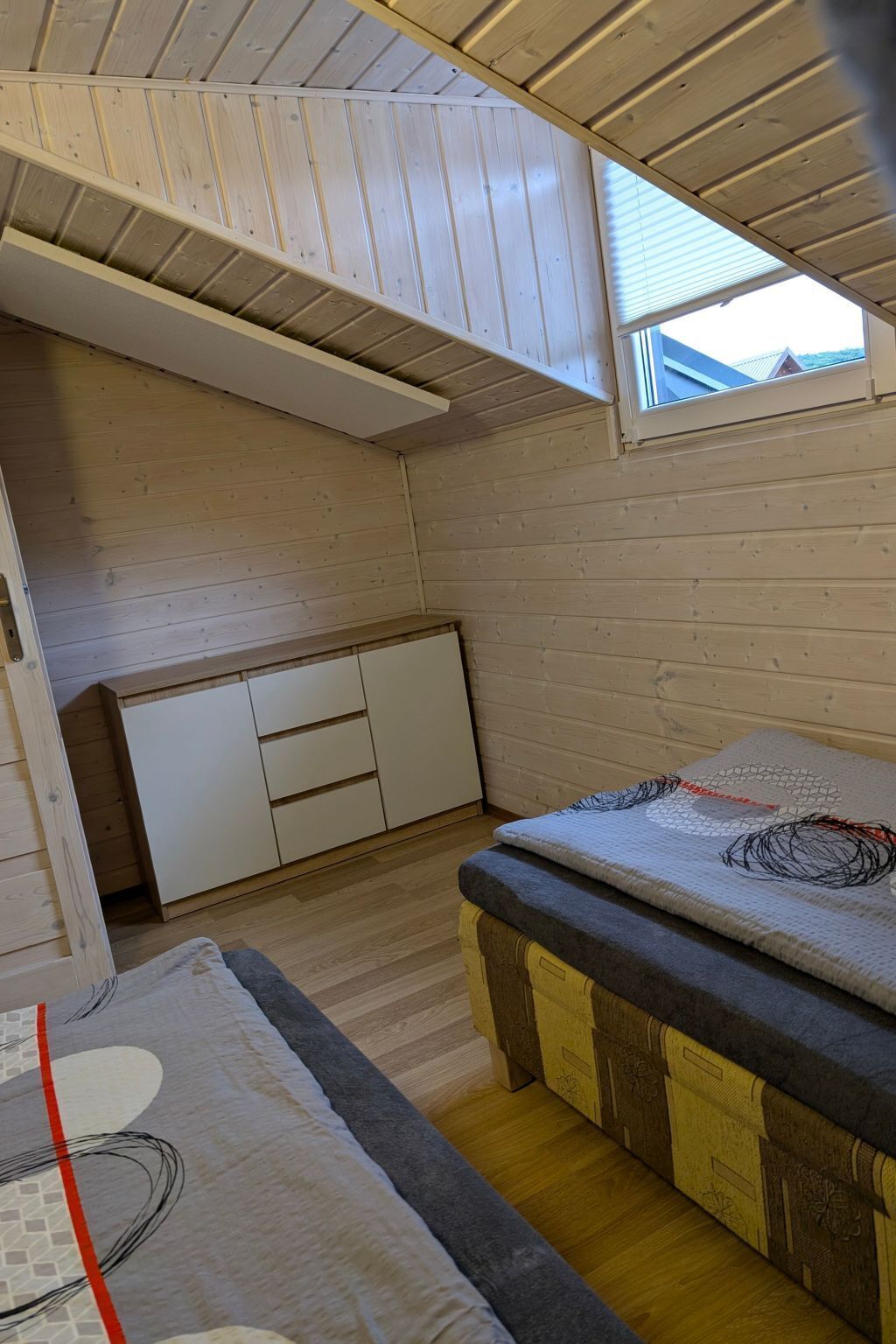 Una stanza compatta con soffitto spiovente, una piccola finestra e un letto con copripiumino decorato.
