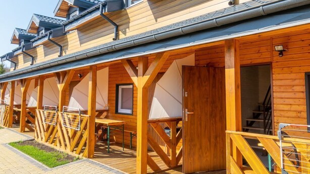A row of wooden cabins with a covered walkway and outdoor seating area. - Trebor"-Häuser in einem eingezäunten Gebiet by Interhome (Miedzyzdroje)