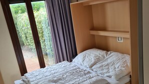 A single bed with a wooden frame and a headboard, a window with curtains, and a view of greenery outside. - Vacation home House by Interhome (Bredene)