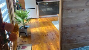 A cozy cabin interior with a wooden floor, a small dining table, a sofa, a kitchen area with cabinets and a refrigerator, and a television mounted on the wall. - Relax’n’Spa by Interhome (Stepnica)
