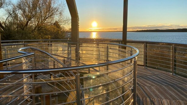 A wooden deck with metal railings overlooking a body of water during sunset. - Haus Kranich by Interhome (Nowe Warpno)