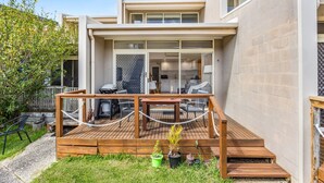 A modern house with a deck, outdoor seating, and a kitchen visible through glass doors. - Coastal Nook (Lorne)