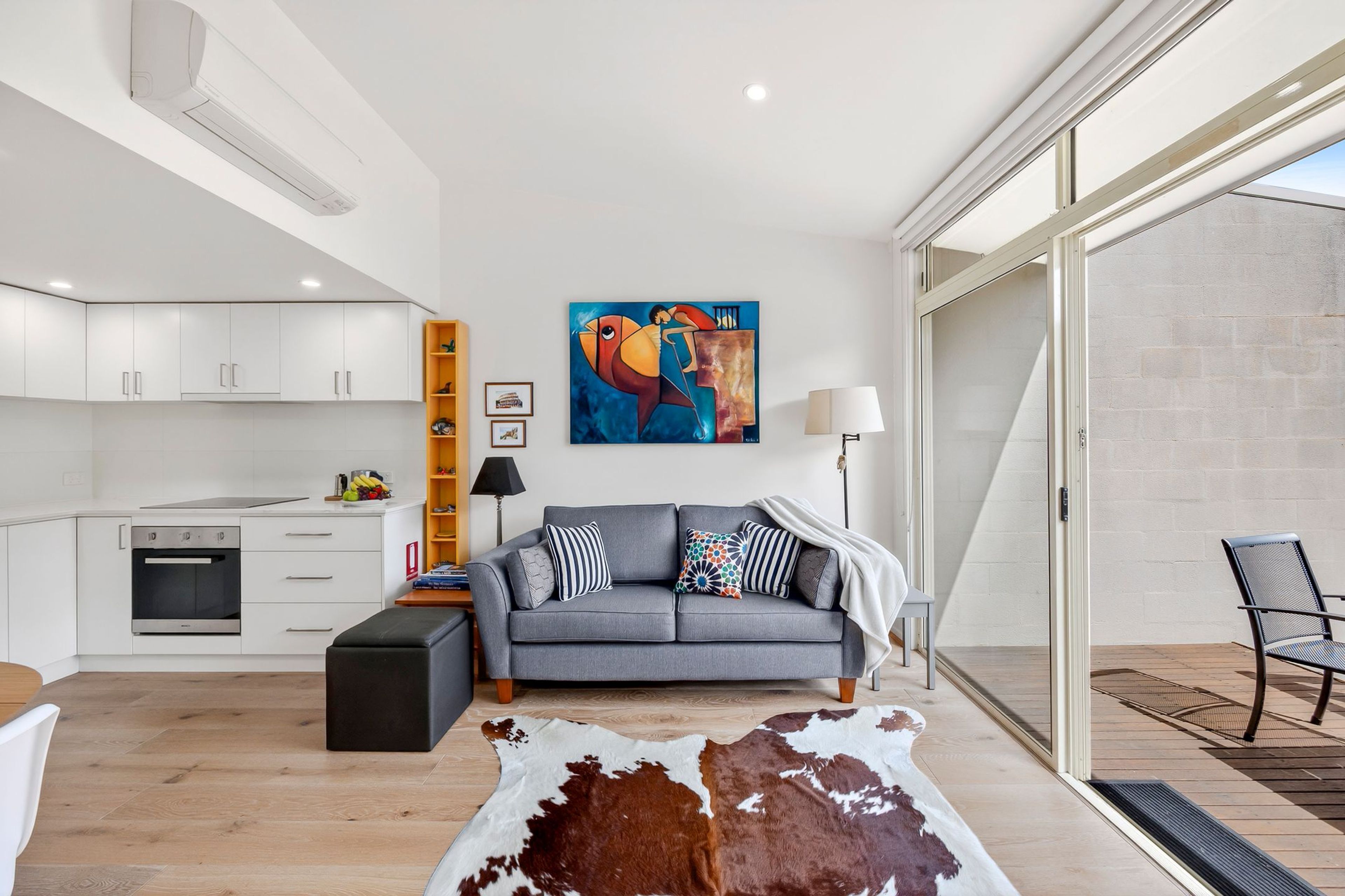 A modern living room with a grey sofa, a cowhide rug, and a painting on the wall.