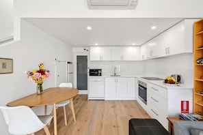 Een moderne keuken met witte kasten, een vaatwasser en een magnetron. Er is een eettafel met stoelen en een bloemenvaas.