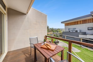 A balcony with a wooden table, a chair, and a bottle of champagne. - Coastal Nook (Lorne)