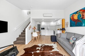 A modern living room with a grey sofa, a brown and white rug, and a flat-screen TV mounted on the wall. - Coastal Nook (Lorne)