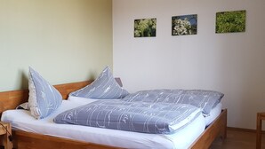 Een houten bed met een grijs-wit beddegoed en kussens, een nachtkastje, en drie ingelijste foto's aan de muur.