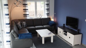 A modern living room with a grey sofa, a white coffee table, a TV on a white cabinet, and a window with curtains. - Traumbrise by Interhome (Rerik)
